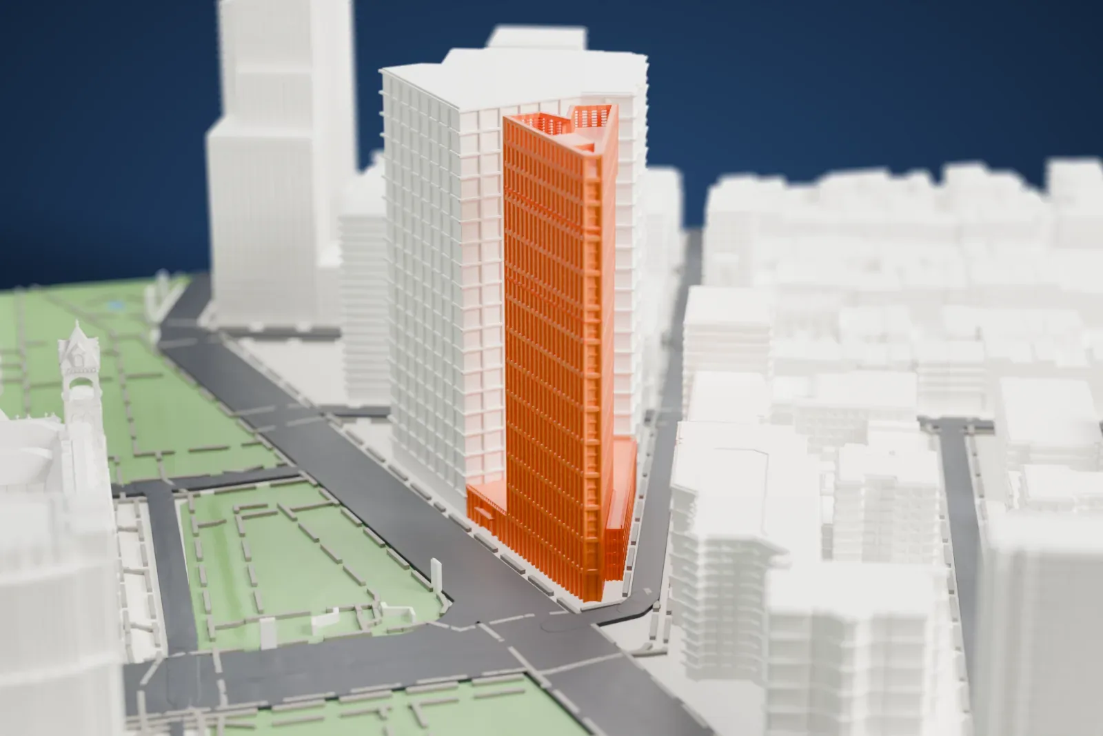 A white 3D print of One Clinton, a tall residential tower with a triangular footprint and a gridded facade, rising among lower buildings with park lawns and streets nearby.