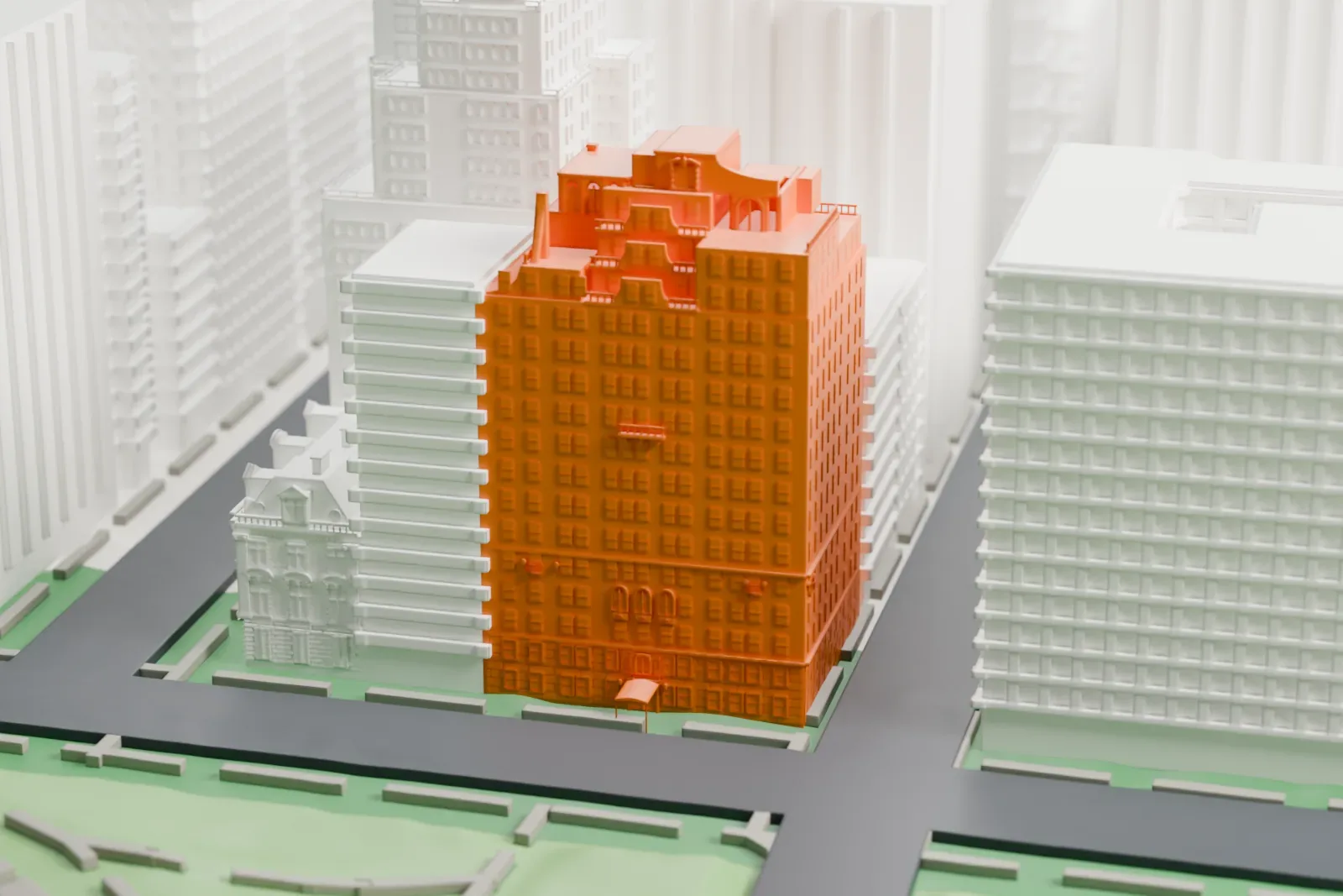 A white 3D print of 1040 Fifth Avenue, a tall apartment building with a stepped roof, standing on a street corner beside a green park.