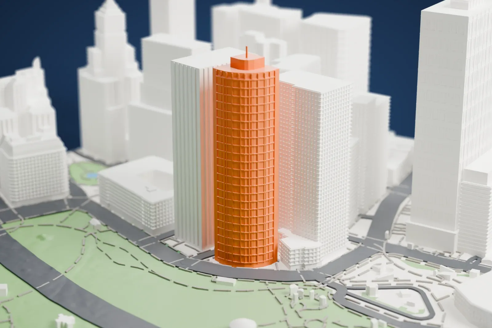 A white 3D print of 17 State Street, a tall tower with a curved front, beside a park with winding paths and a strip of water, among other tall buildings.