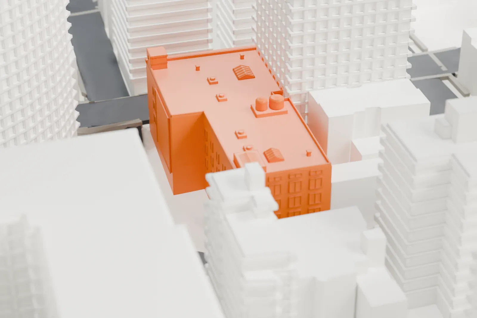 A white 3D print of 207 East 36th Street, a flat-roofed building with rooftop water tanks, wedged between much taller neighboring buildings above a street.