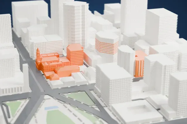 A white 3D print of Adelaide Town Hall, a long building with pitched roofs and a slim clock tower with a domed top, hemmed in by taller gray buildings and city streets.