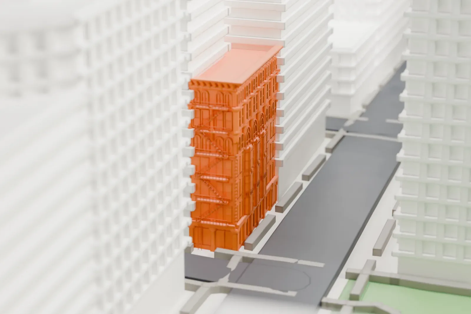 A white 3D print of the Ahrens Building, a tall narrow building with fire escapes on its face, squeezed between much taller buildings above a street.