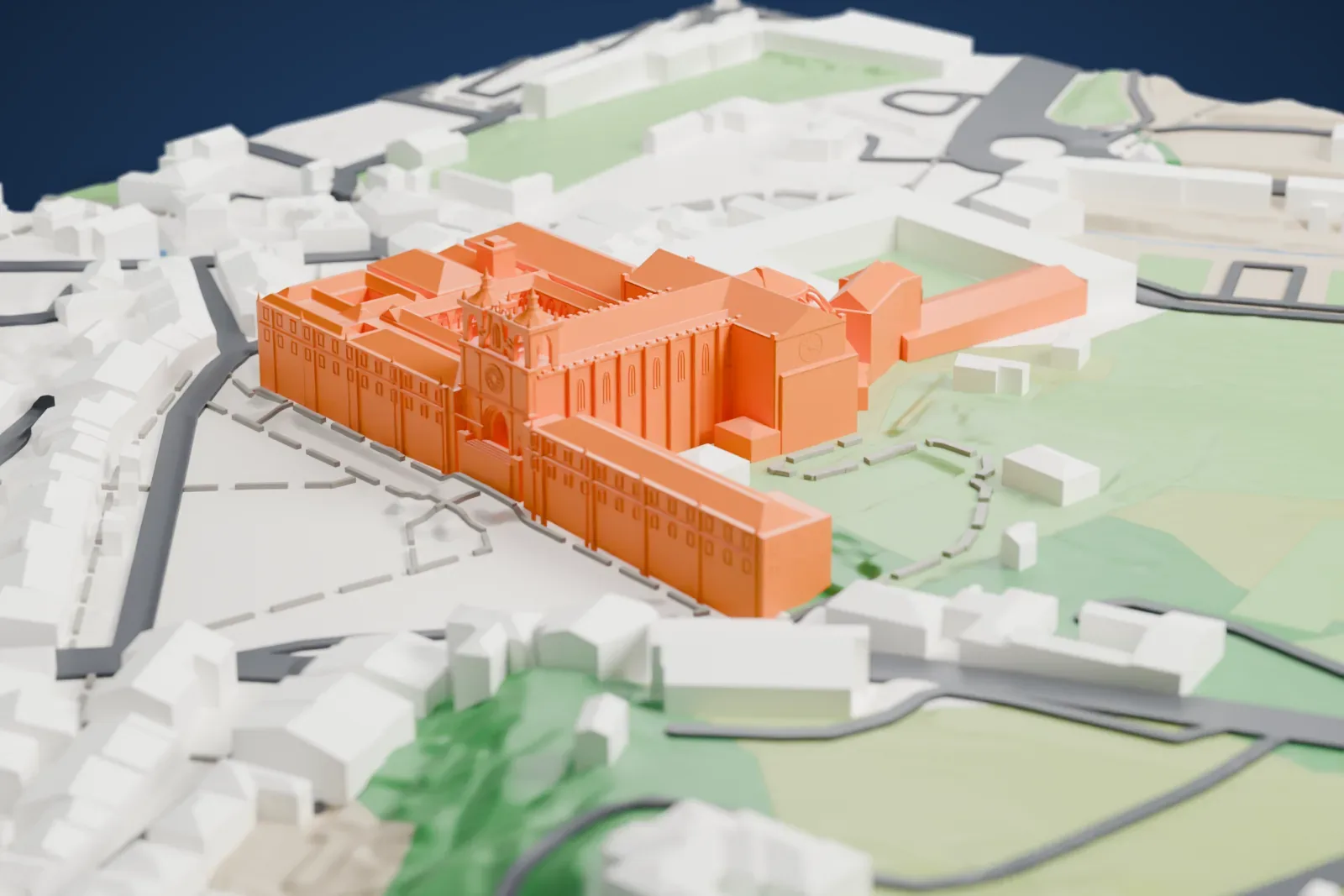 A white 3D print of the Alcobaça Monastery, a long church with a rounded apse and two towers beside long monastery wings, with the town's buildings and green hillside around it.