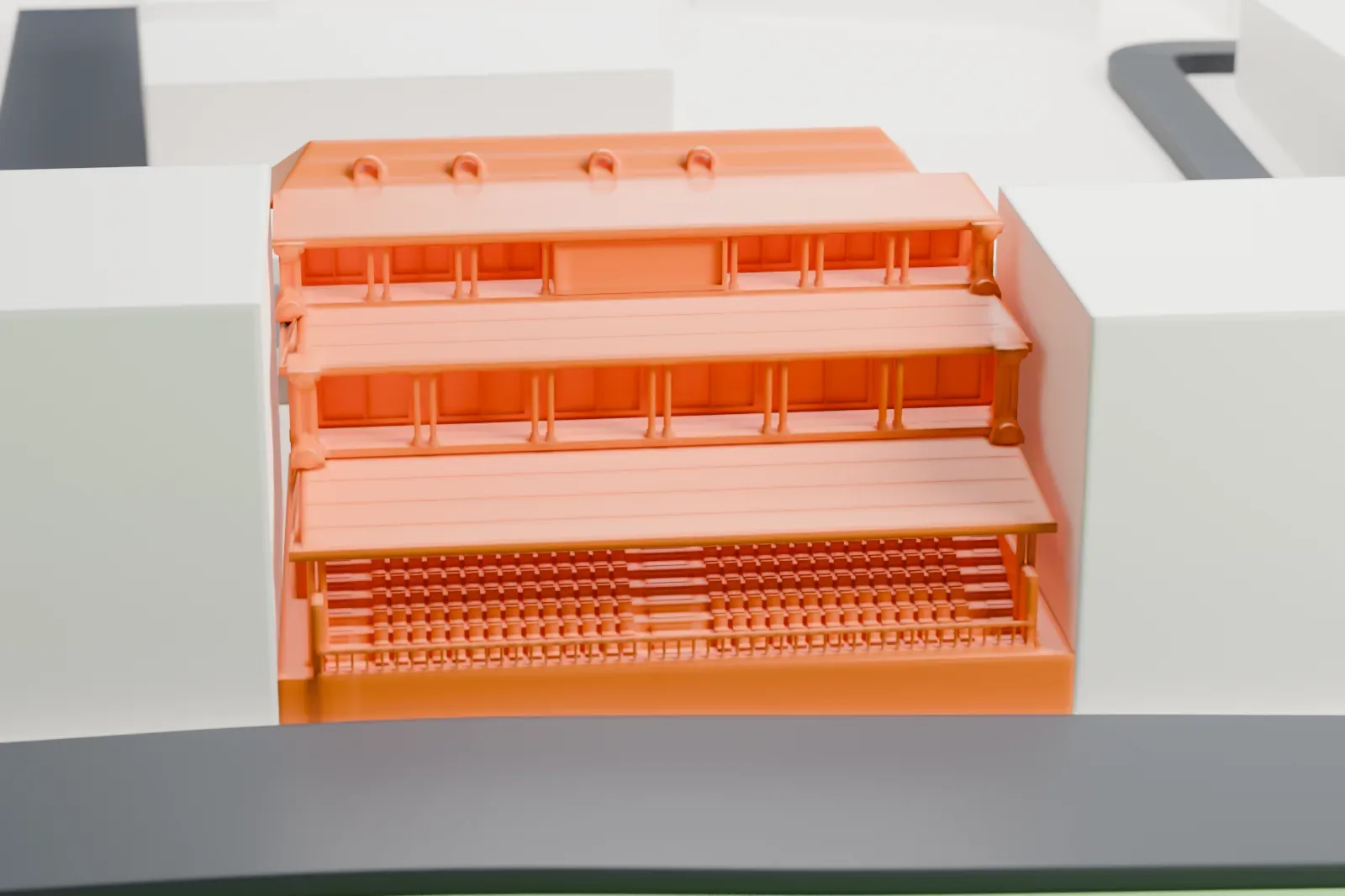 A white 3D print of Alexandria Stadium's stepped grandstand, with tiered roofs and rows of seats, between larger buildings and streets.
