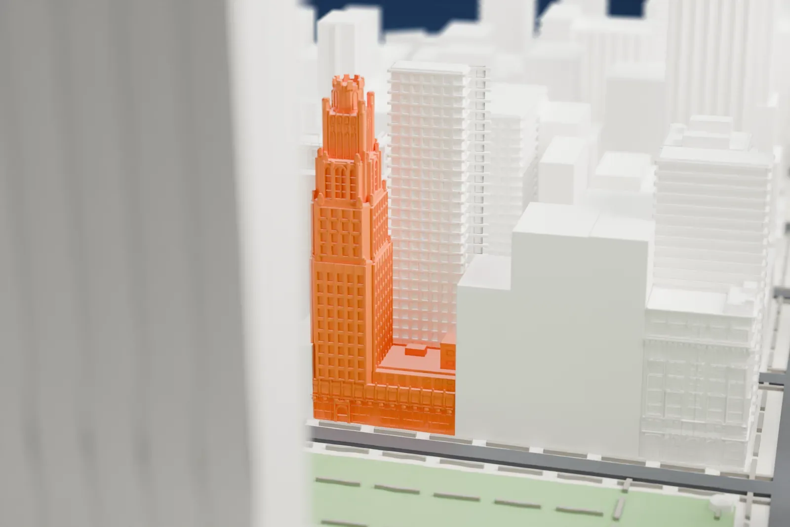 A white 3D print of the American Radiator Building, a tall stepped tower with a pointed crown, standing beside a small park among taller and shorter Midtown buildings.