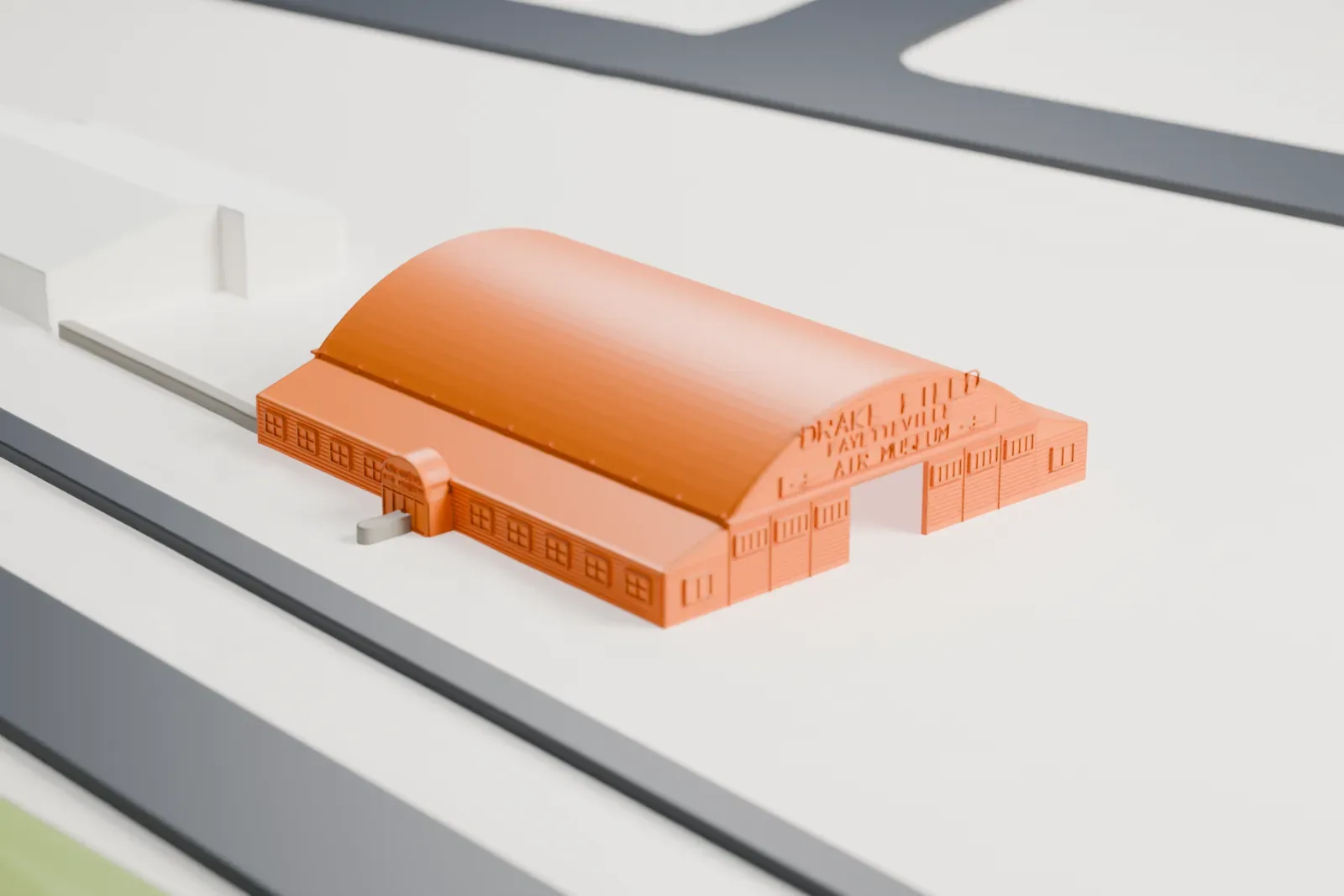 A white 3D print of the Arkansas Air & Military Museum Historic Wooden Hangar, with its surrounding area.