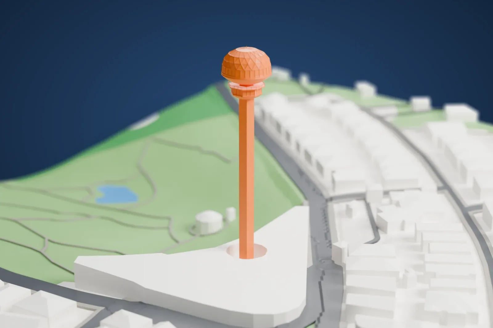 A white 3D print of Atakule, a slender square tower topped by a domed crown, rising from a wide low building with houses, roads and green patches around it.