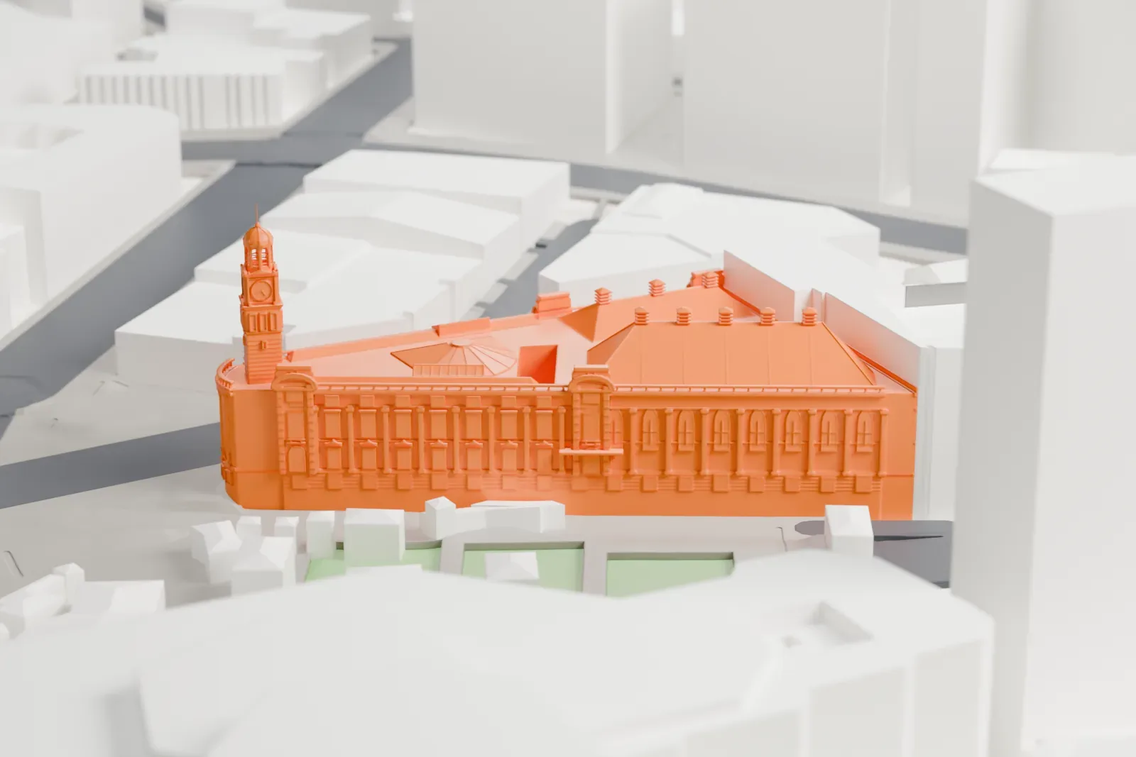 A white 3D print of Auckland Town Hall, a corner building with a clock tower, pitched roofs with small chimneys and a columned curved corner, among taller buildings.
