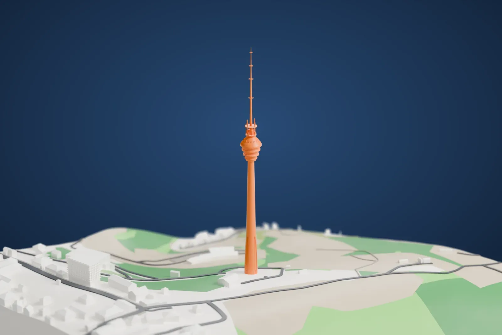 A white 3D print of the Baku TV Tower, a slender concrete tower with a rounded pod and a tall mast, above the surrounding land and buildings.