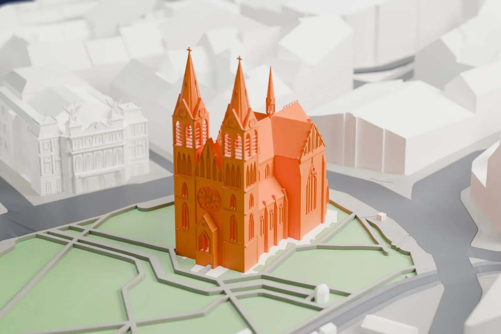 A white 3D print of the Basilica of St. Ludmila with its two towers, standing among the surrounding streets and buildings.