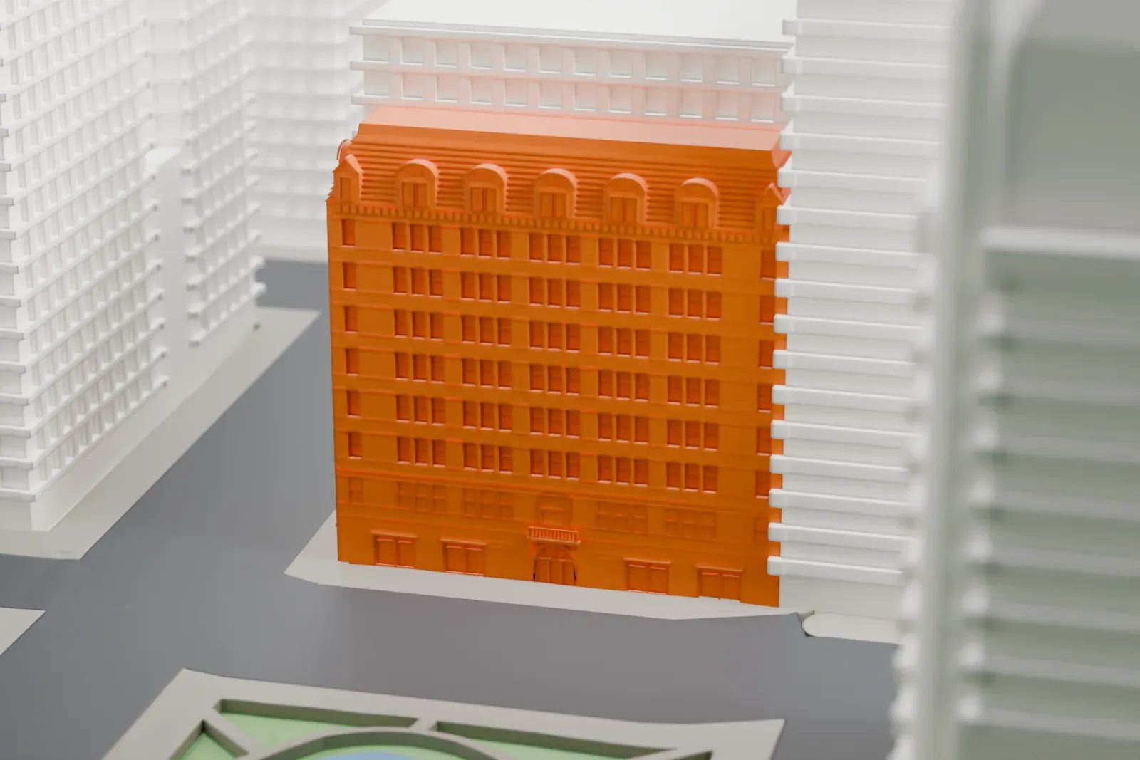 A white 3D print of the Bergdorf Goodman Building, a narrow building among taller towers, with a park and pond close by.