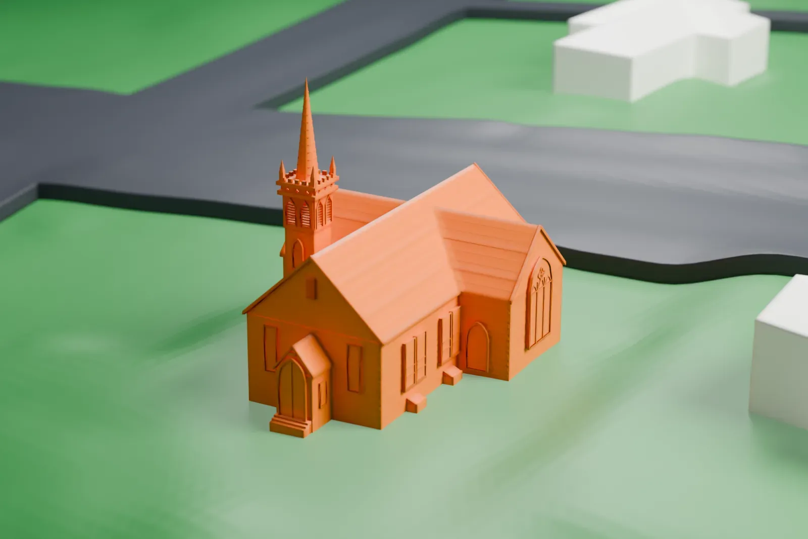 A white 3D print of a small chapel with a steeple, standing among houses on a green hillside.