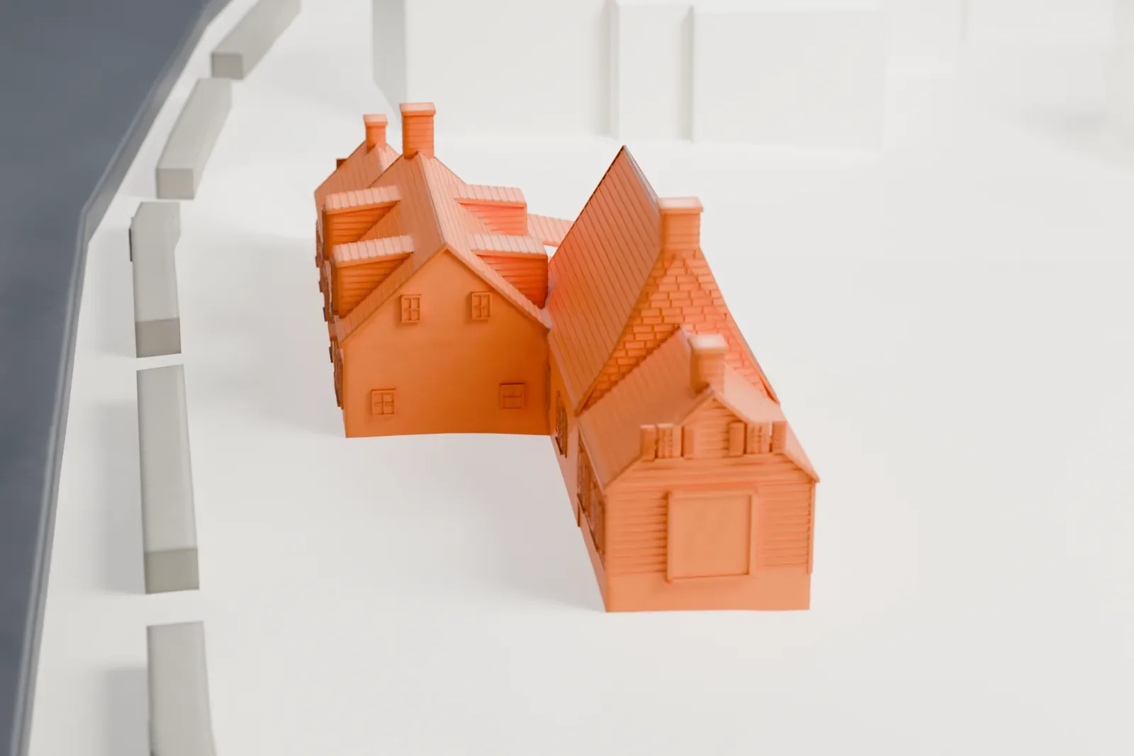 A white 3D print of the Billiou-Stillwell-Perine House, a low house with several sloping shingled roofs, dormers, chimneys and a small porch, beside a road with a few buildings nearby.