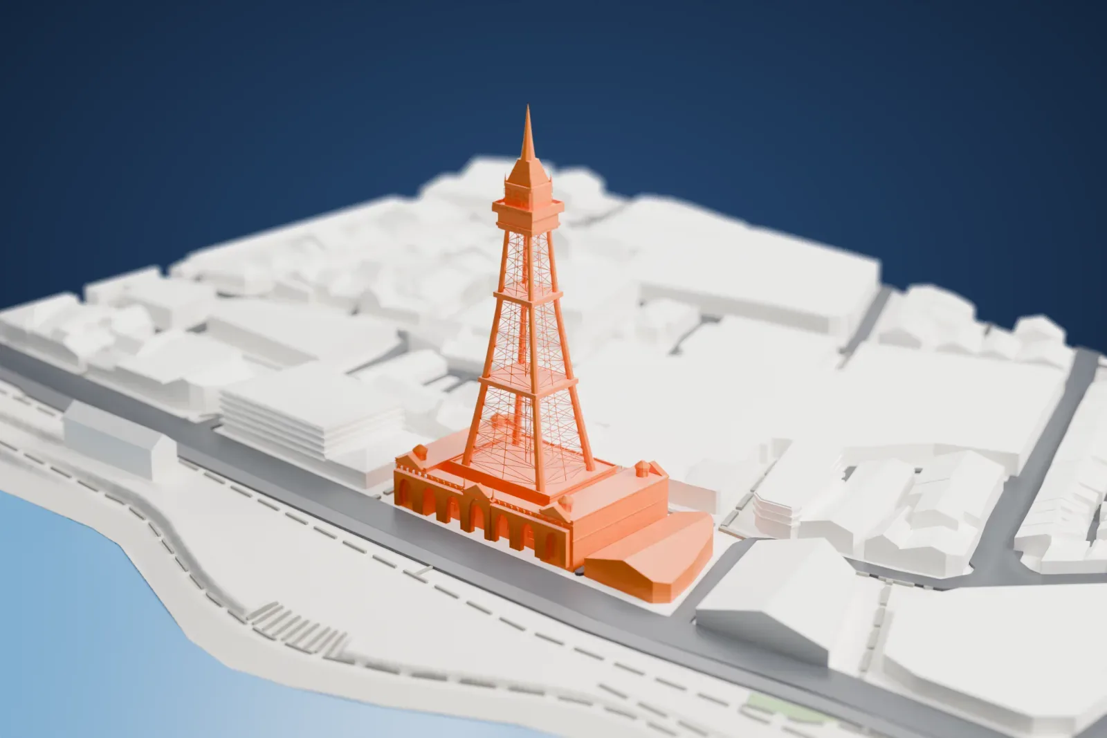 A white 3D print of Blackpool Tower, a tall lattice tower with a spire rising from a base building with four corner domes, with the sea and a wide road beside it and city blocks behind.