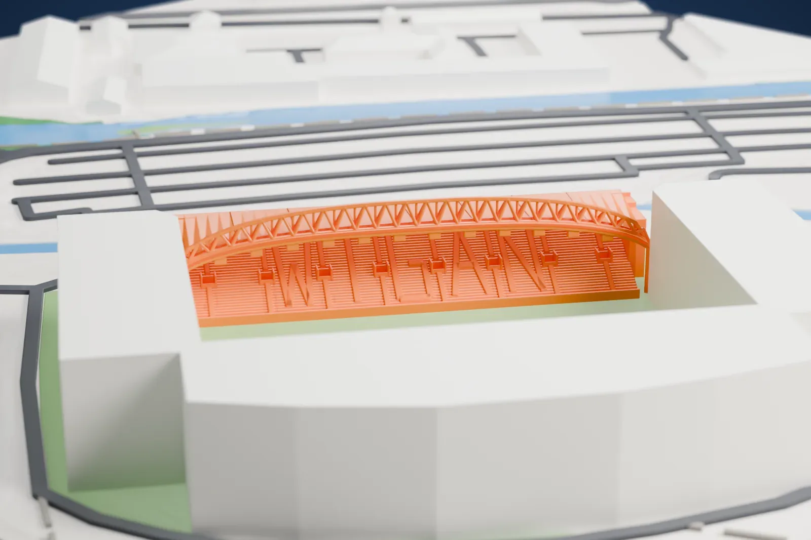 A white 3D print of the East Stand at Brick Community Stadium, a long single-tier stand under an arched roof truss, with the surrounding city around it.