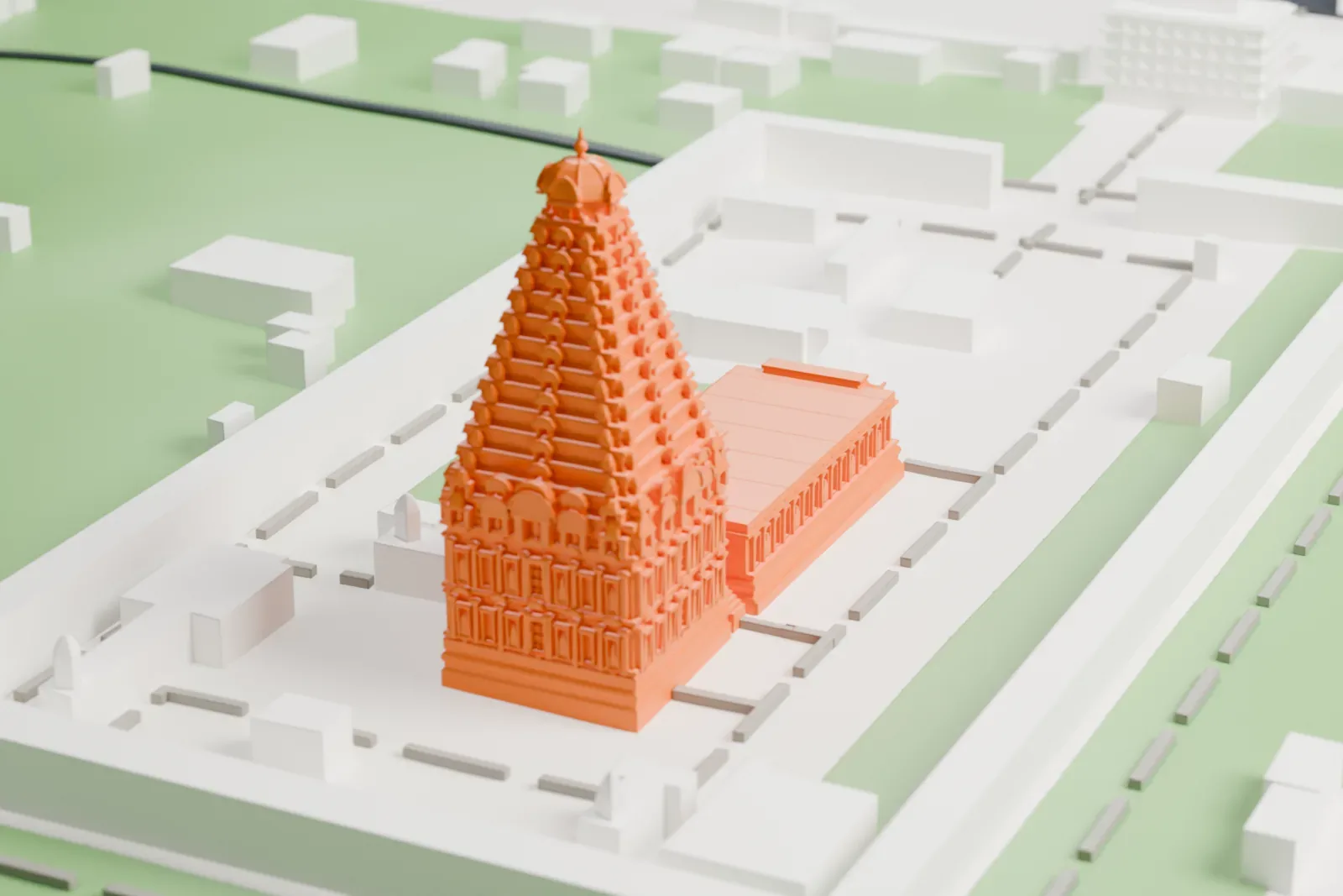 A white 3D print of Brihadisvara Temple, a tiered pyramid-shaped tower beside a long flat-roofed hall inside a rectangular walled courtyard, with a river, green lawns and low buildings nearby.
