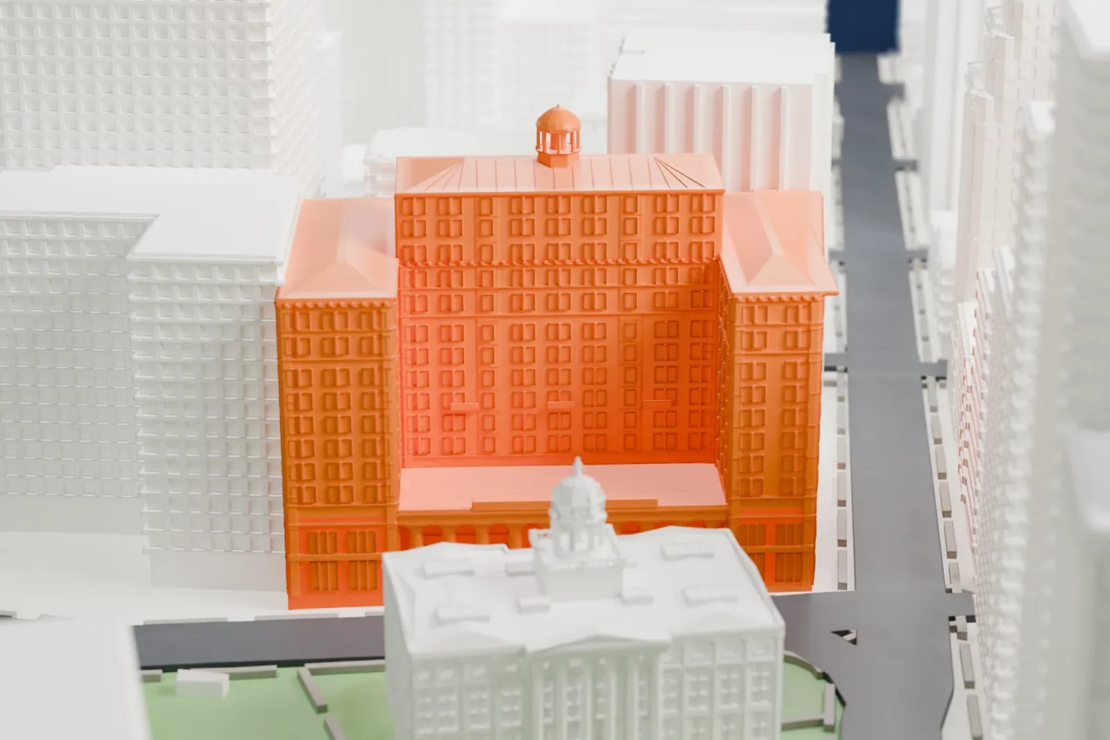 A white 3D print of the Brooklyn Municipal Building, a tall civic building with a small domed cupola on its roof, among taller buildings, streets and green space.