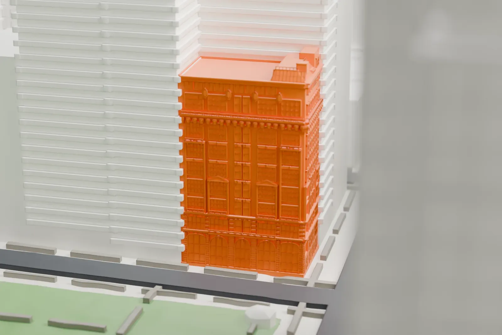 A white 3D print of the Bryant Park Studios, a tall narrow building with an ornate roofline on a street corner beside a green park.