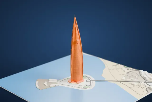 A white 3D print of the Burj Al Arab, a tall sail-shaped tower on a small round island with a curving road, surrounded by sea with a shoreline and a few buildings beyond.