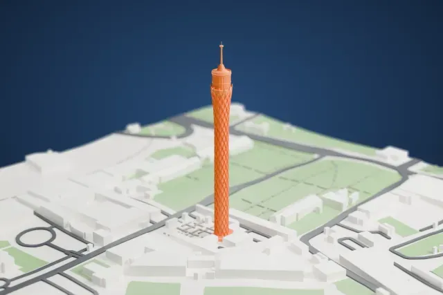 A white 3D print of the Cairo Tower, a slender lattice tower with a round deck and a thin spire, standing among buildings, roads and green parks.
