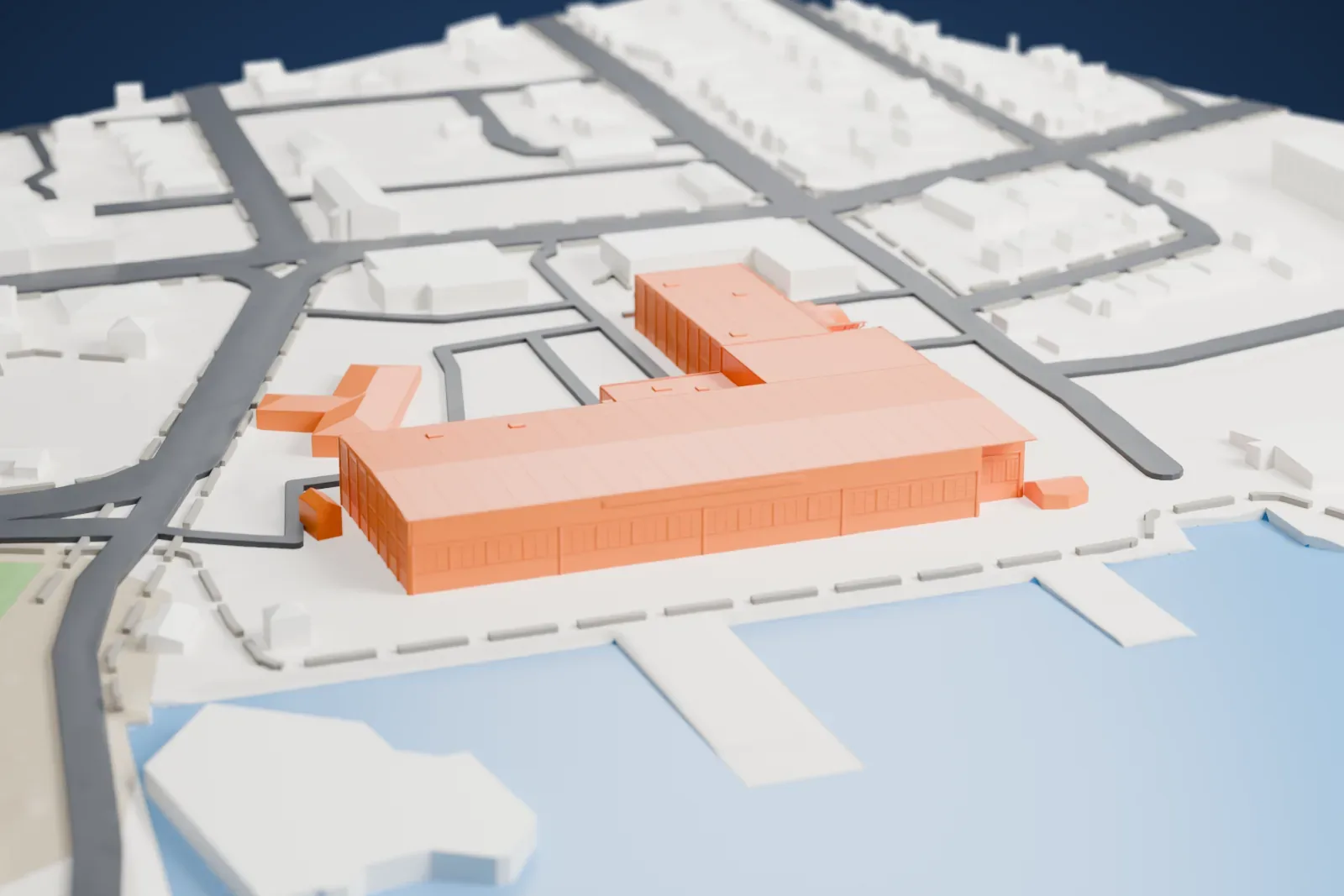 A white 3D print of the CBHC bush plane museum hangar, a wide L-shaped building beside water with small piers, surrounded by streets and small buildings.
