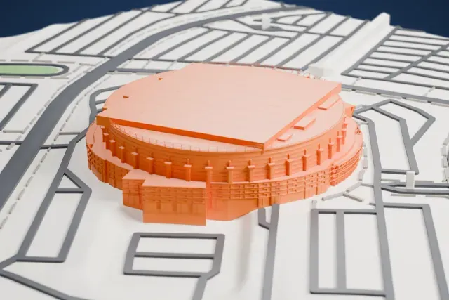A white 3D print of the Canadian Tire Centre, a round arena with a broad flat roof and a ring of columns around its walls, surrounded by wide roads and open ground.