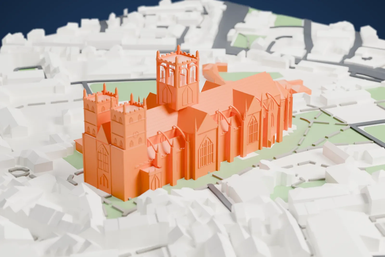 A white 3D print of Canterbury Cathedral, a long church with a tall central tower, towers at the west end and a rounded east end, among dense buildings, green lawns and paths.