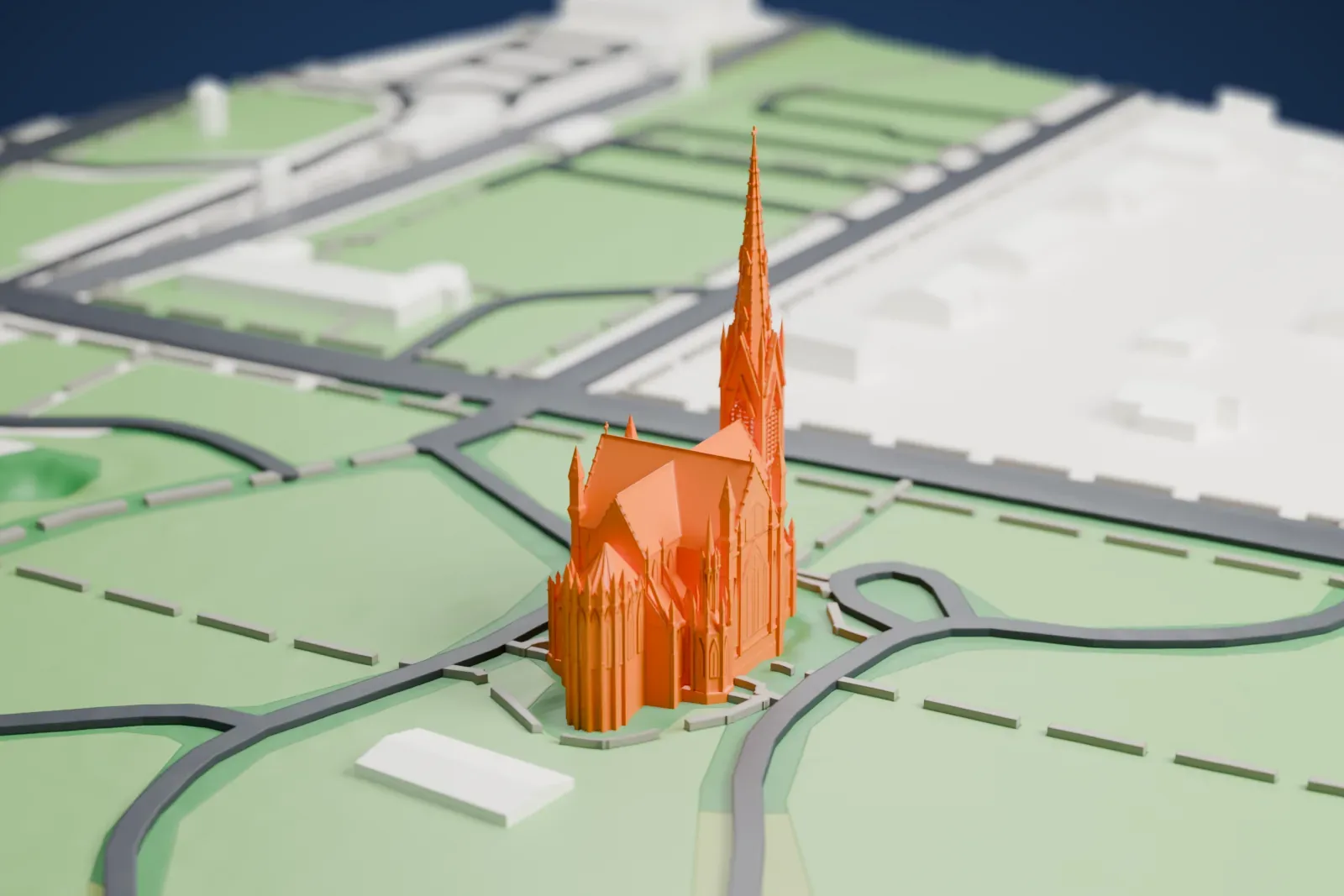 A white 3D print of the Cathedral of the Incarnation, a Gothic church with a tall spire and many pinnacles, on green grounds ringed by curving roads.