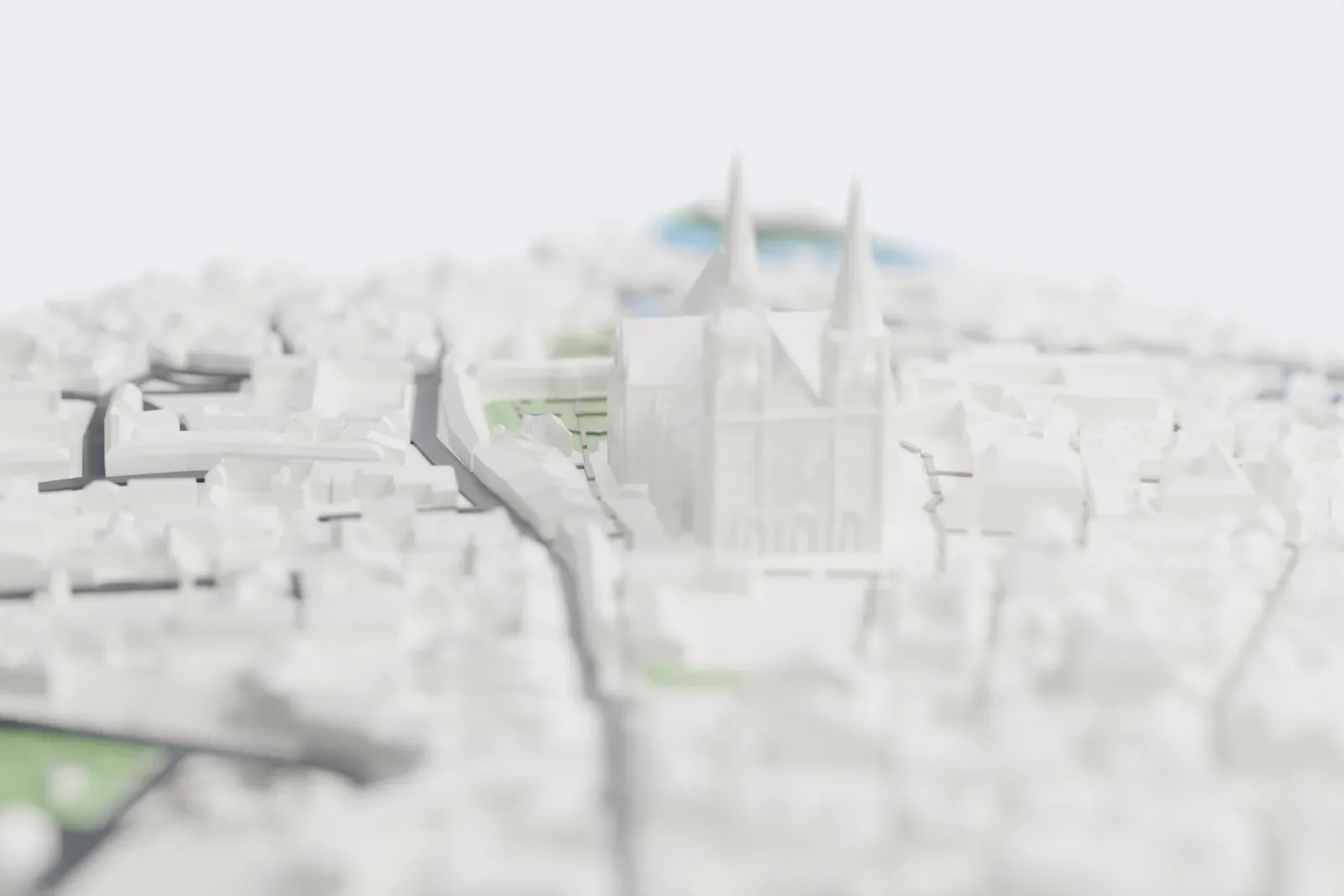 A white 3D print of Chartres Cathedral, a long Gothic church with two tall spires at one end, flying buttresses along its sides and a rounded east end, set among dense town buildings beside a green slope.