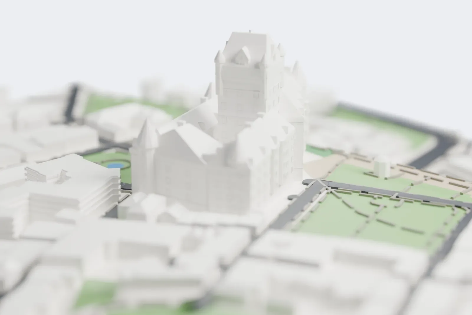 A white 3D print of the Château Frontenac, a hotel of several wings around a tall central tower, with steep roofs and cone-topped turrets, beside lawns and paths at the edge of a cliff with city buildings around it.