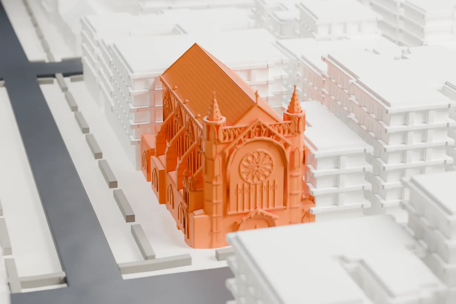 A white 3D print of the Church of the Incarnation, a long stone church with a steep roof and two small pointed towers, among taller buildings and streets.