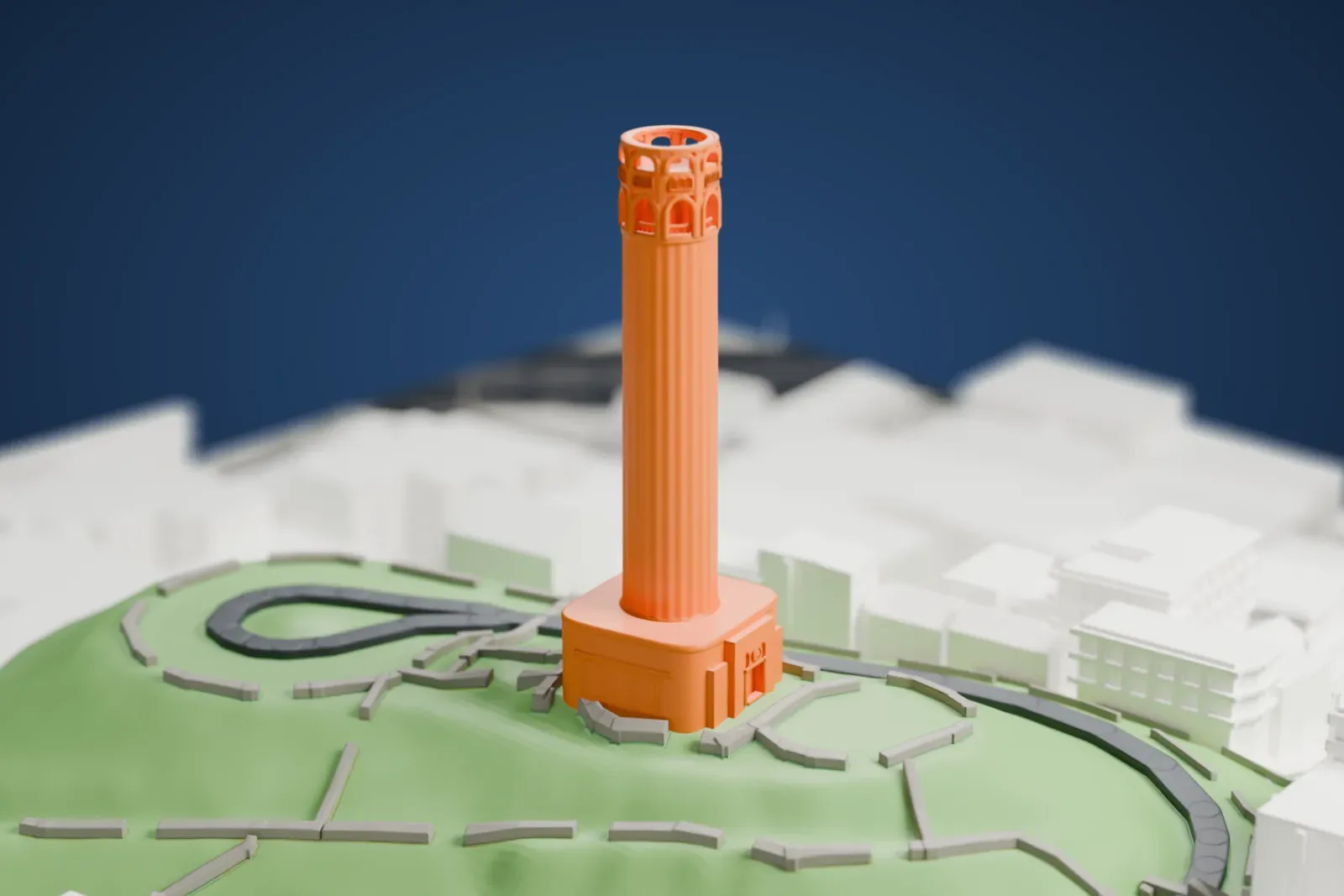 A white 3D print of Coit Tower, a tall fluted round tower on a square base with an arcade near the top, standing on a green hilltop with a looping road and city buildings around it.