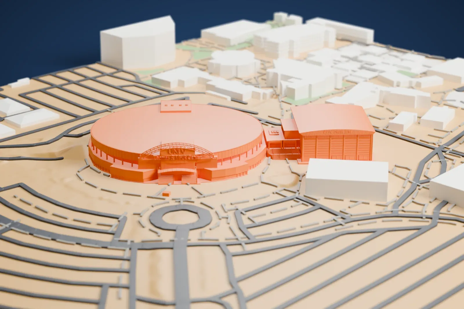 A white 3D print of Cox Pavilion, a boxy arena with a gently curved roof and finely lined walls, standing beside a larger curved building and a tangle of roads.