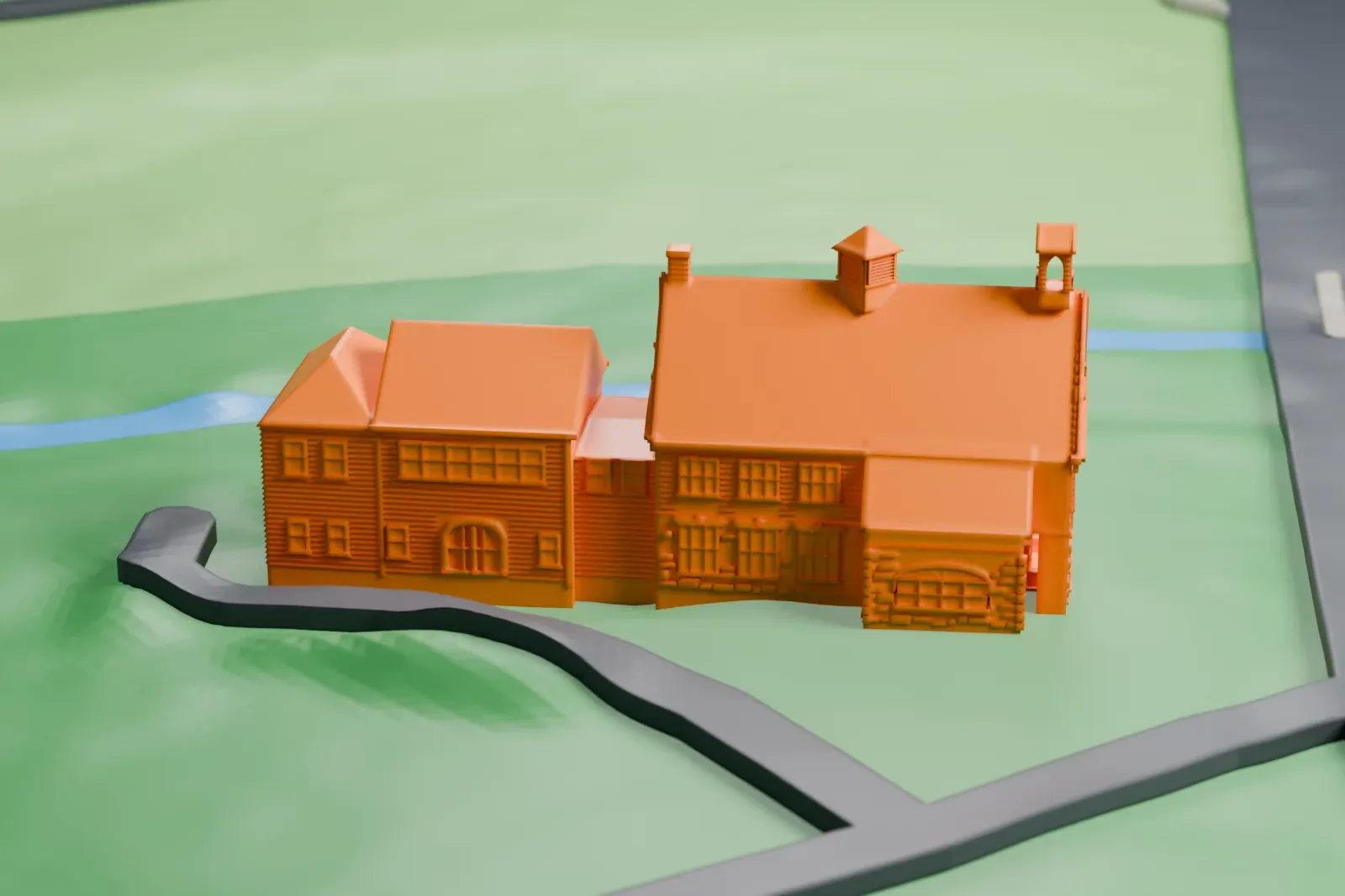 A white 3D print of a schoolhouse with small bell cupolas and steep gables, beside a stream and green lawns.