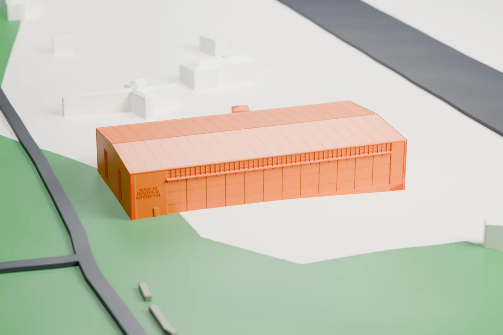 A white 3D print of the Hellenic Air Force Museum hangar, a large, low building with a ridged roof and small windows on its end walls, standing on open ground with a road and a few small buildings nearby.