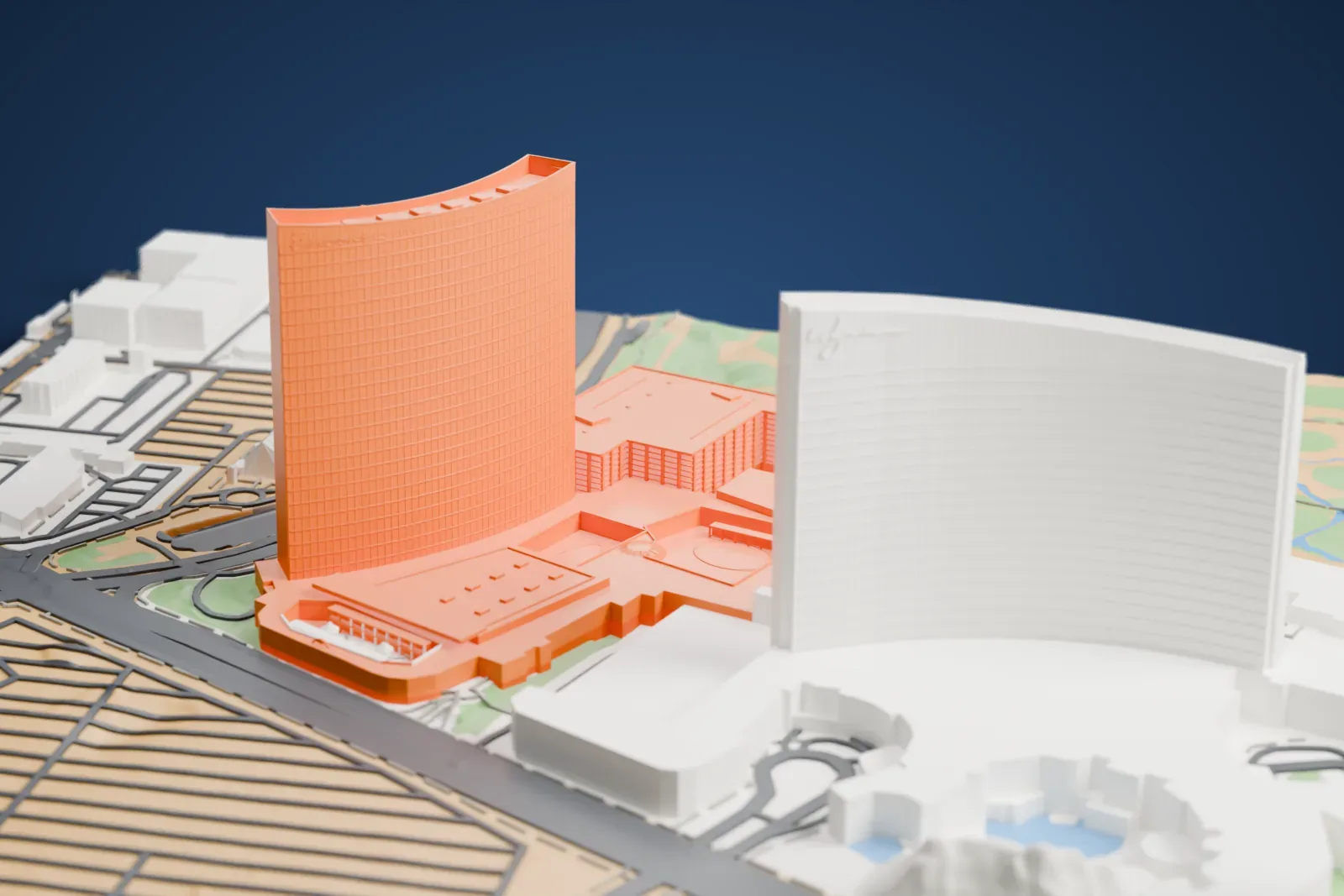 A white 3D print of Encore Las Vegas, a tall curved hotel tower with low wings at its base, standing beside a second curved tower with roads and green land around them.
