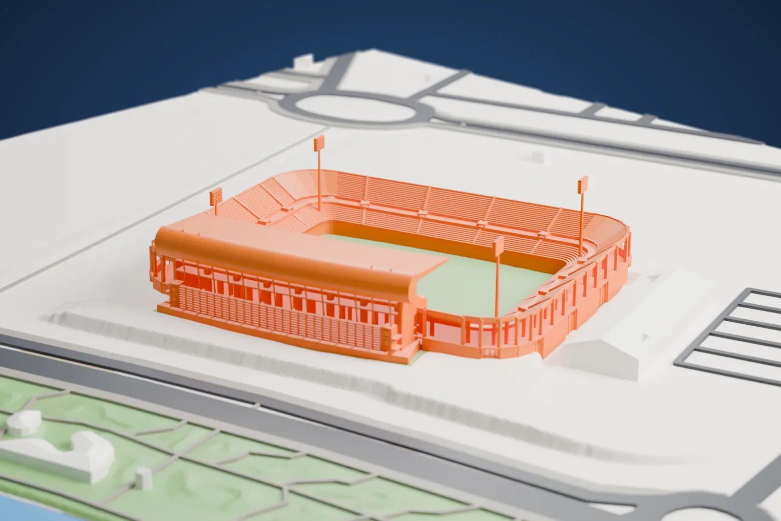 A white 3D print of Estadio Nuevo Colombino, a stadium with a covered stand and four floodlight masts, on open ground beside roads, a strip of green and water.