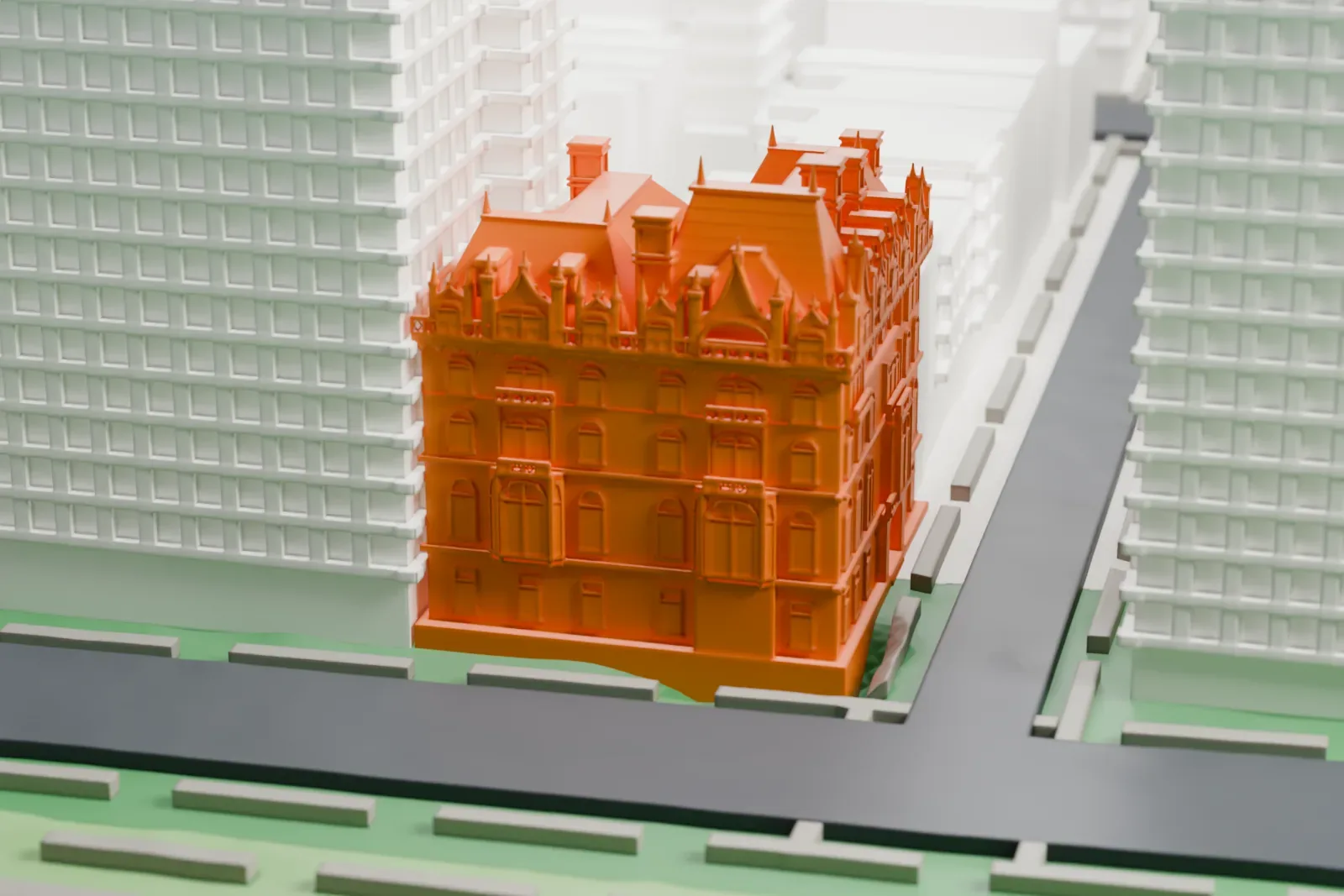 A white 3D print of the Felix M. Warburg House, a corner mansion with a steep roof, dormers and chimneys, beside a street and tall buildings.