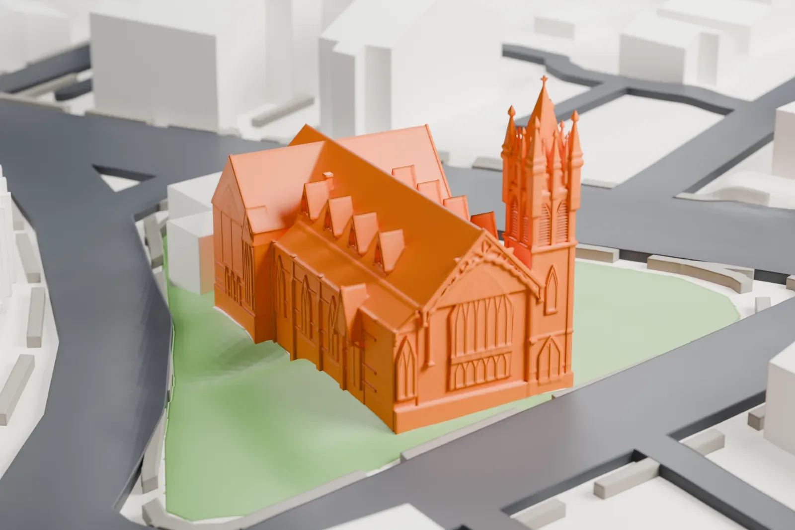 A white 3D print of the First Baptist Church of Ossining, a T-shaped gabled church with a tall pinnacled steeple, on a small green lot at a street junction.