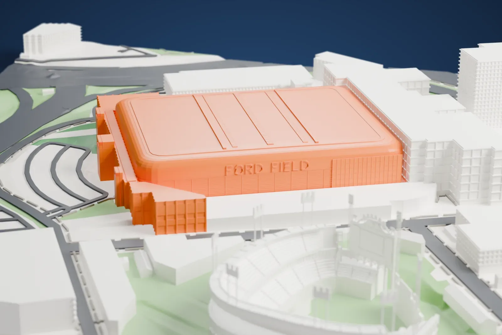 A white 3D print of Ford Field, a long rounded stadium with a tall ribbed wall and a low domed roof, surrounded by city blocks and streets.