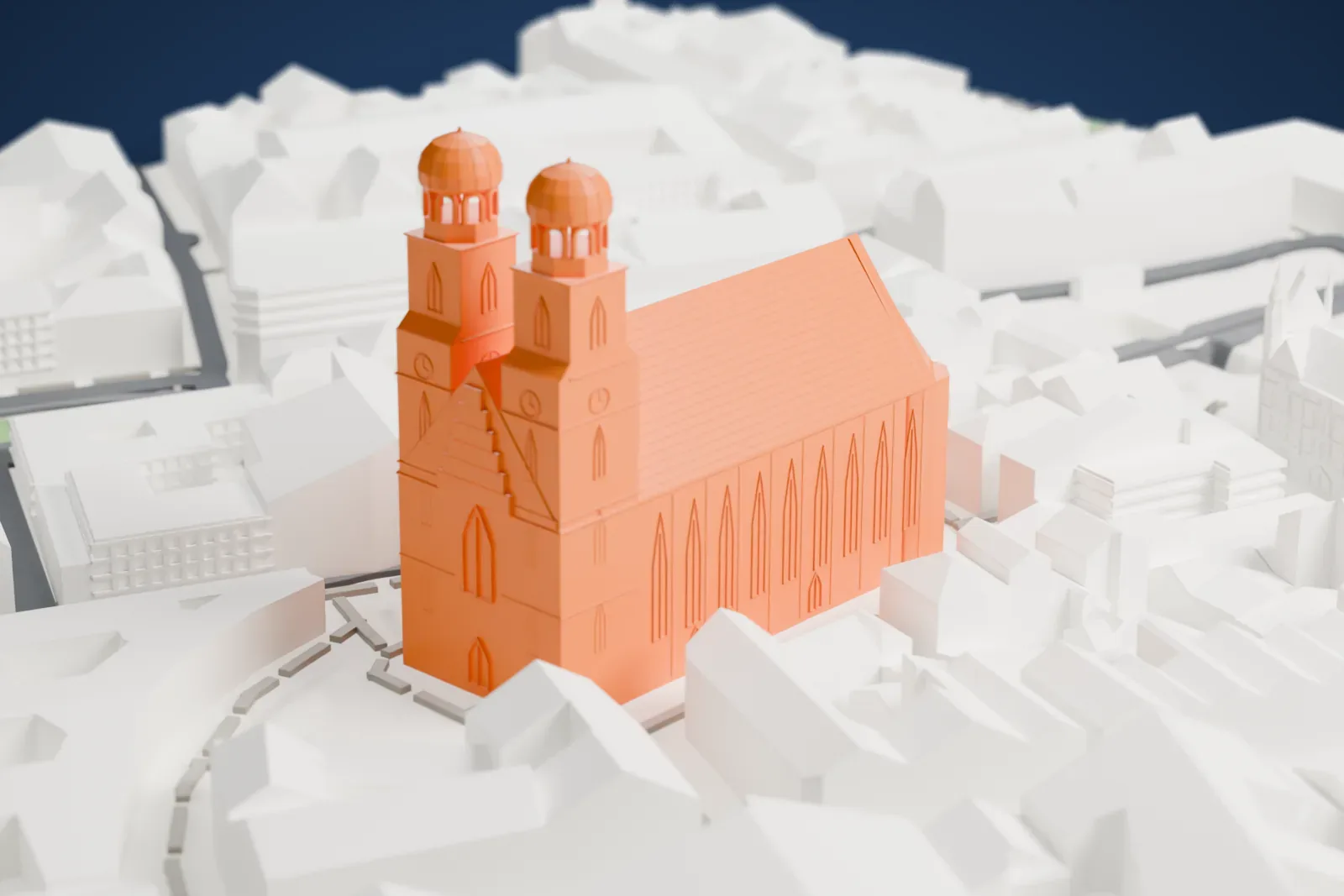 A white 3D print of the Frauenkirche in Munich, a long church with a steep roof and two domed towers, packed in by the surrounding buildings and streets.