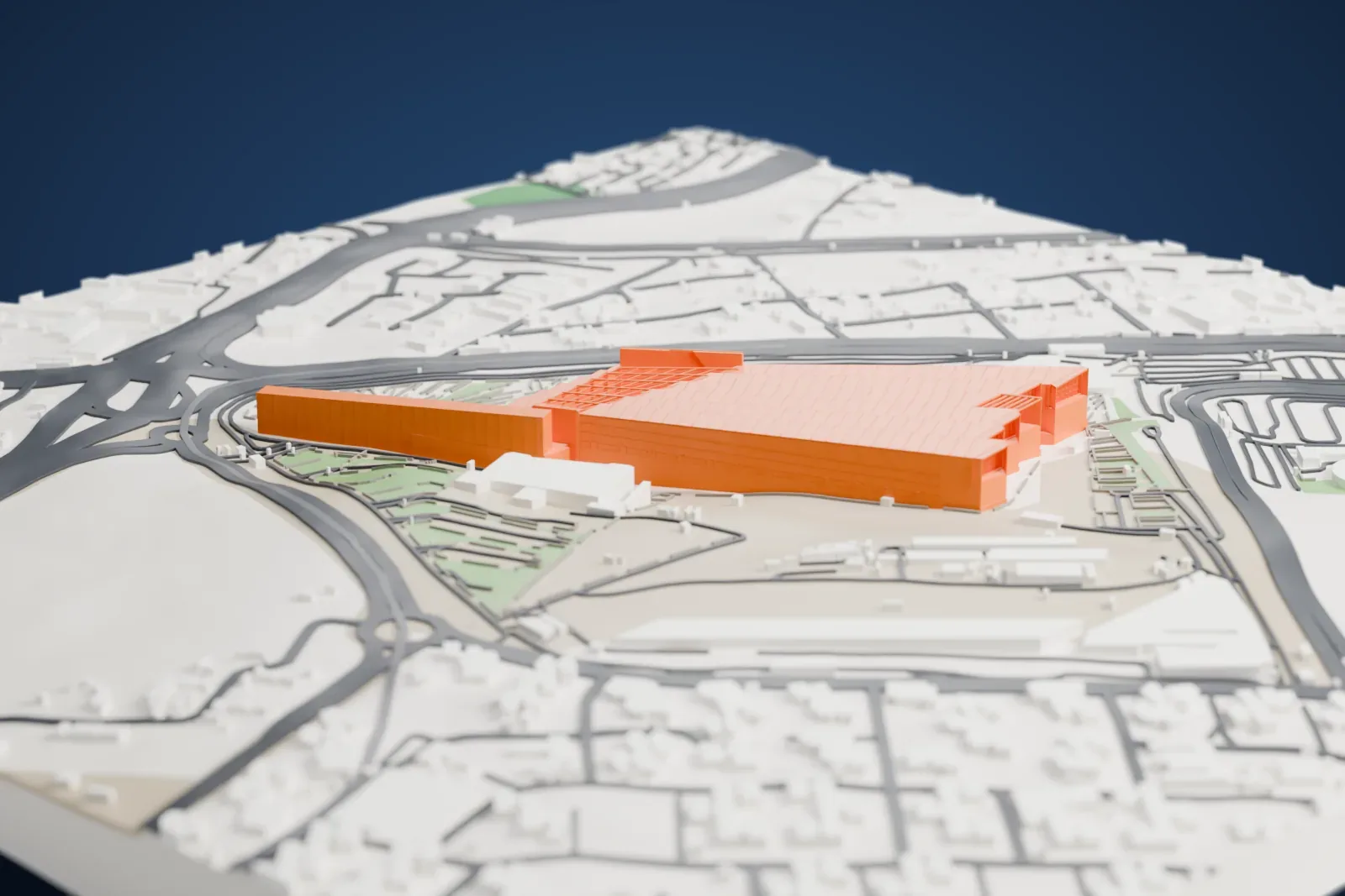 A white 3D print of the Grand Egyptian Museum, a long, low wedge-shaped building with a ribbed roof, on open ground ringed by roads and low buildings.