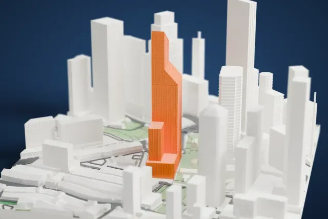 A white 3D print of Guoco Tower, a tall slim tower with an angled, finned top, standing among neighboring high-rises, small parks and streets.