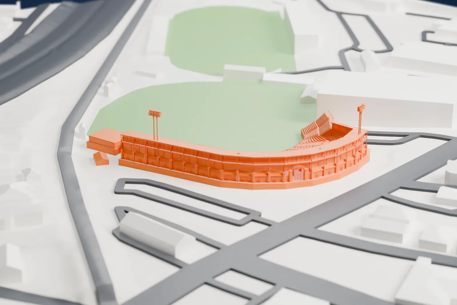 A white 3D print of Hadlock Field, a baseball stadium with a curved grandstand and tall floodlight towers around a grass field, beside roads and large flat-roofed buildings.