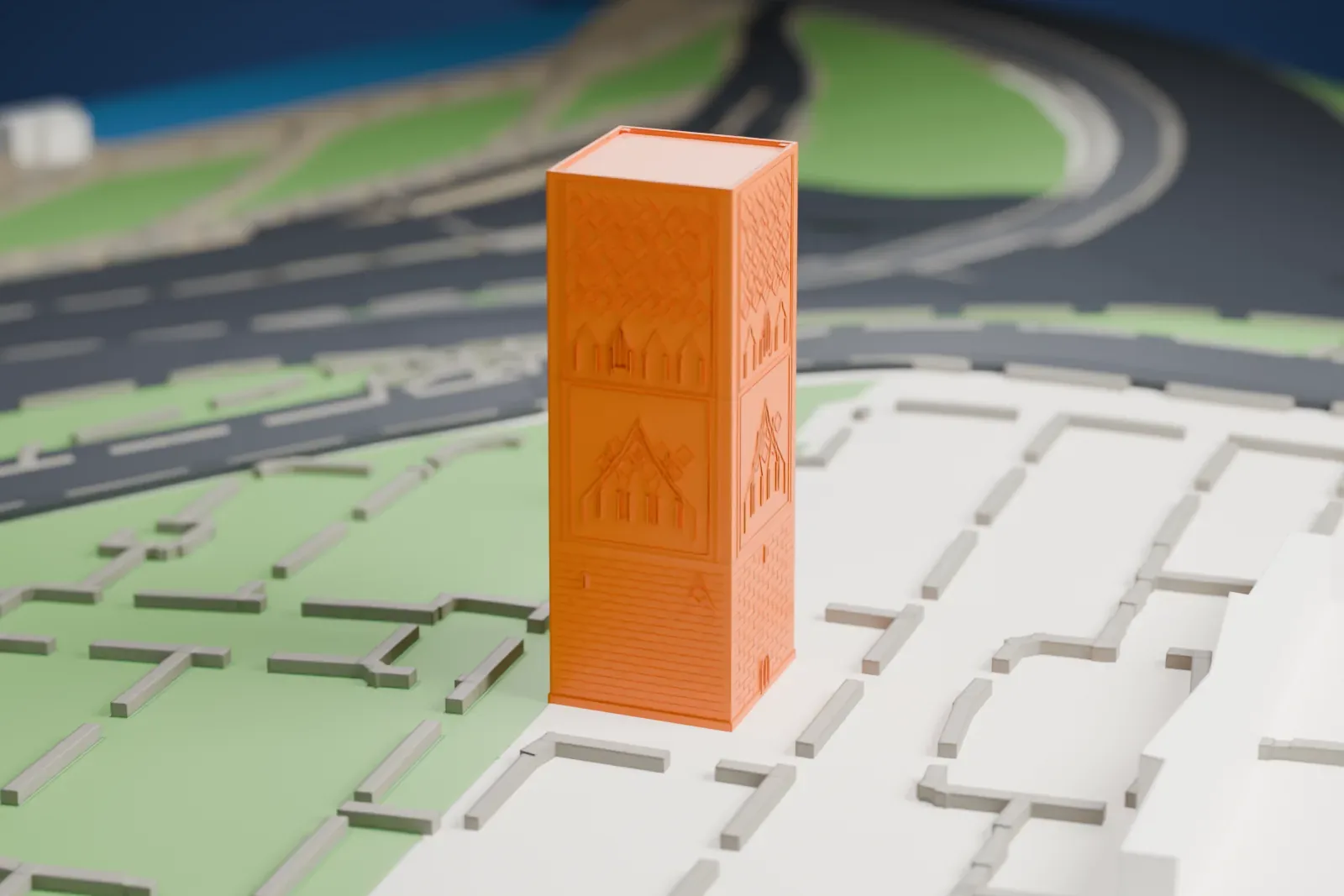 A white 3D print of the Hassan Tower, a square tower with patterned relief panels and a brick-like base, standing alone on open ground beside a road.