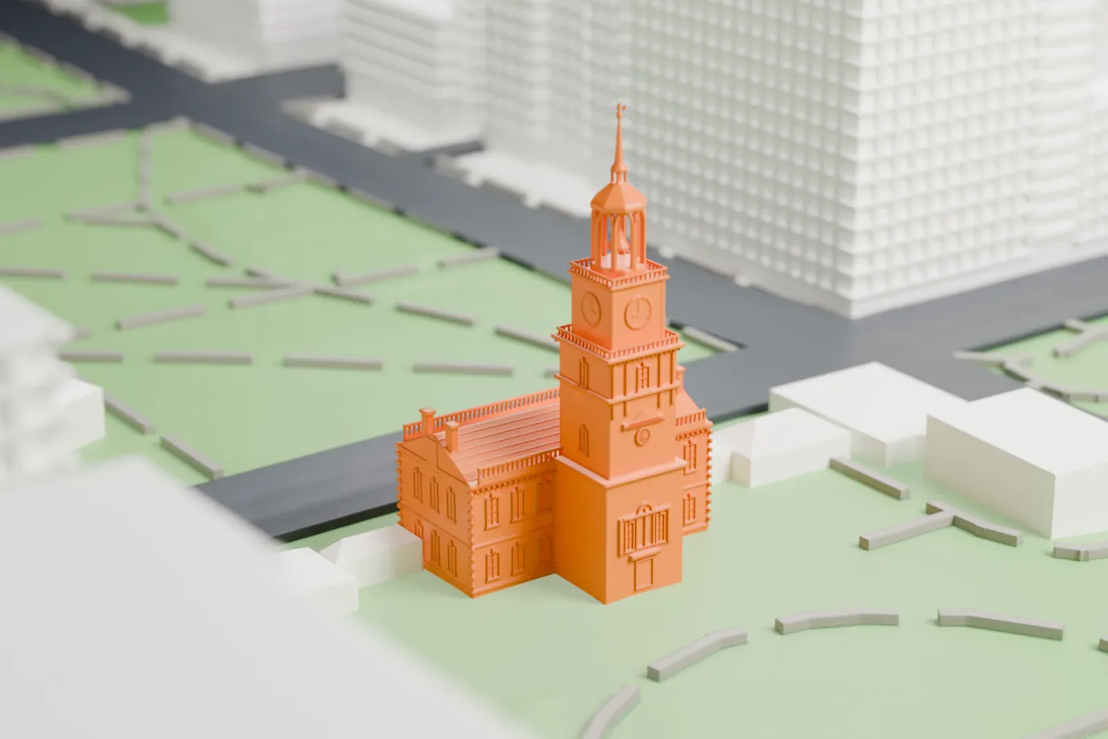 A white 3D print of Independence Hall, a long building with a clock tower and slim spire, standing on a green lawn with curved paths, with streets and large buildings around it.