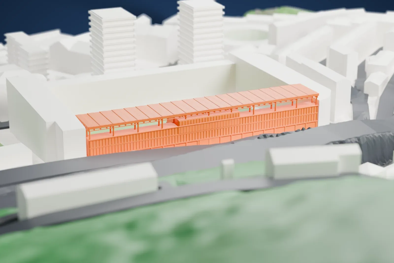 A white 3D print of Ipurua Municipal Stadium, a steep single tier of seats under a long flat truss roof, with a row of glazed boxes along its back, among the surrounding streets and buildings.