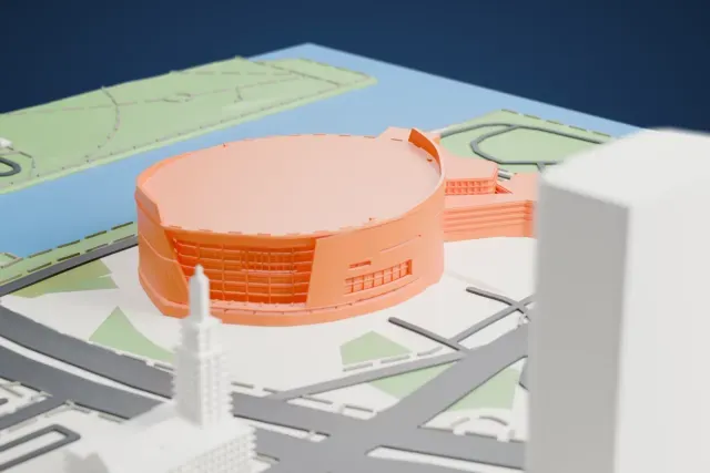 A white 3D print of Kaseya Center, a round arena with a broad flat roof and a glazed section on its curved wall, beside a patch of water with roads, parks and a few buildings around it.