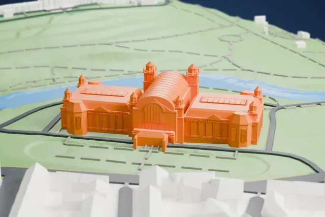 A white 3D print of Kelvingrove Art Gallery and Museum, a broad building with a barrel-vaulted central roof and small domed turrets, set in a green park beside a river, with city streets beyond.