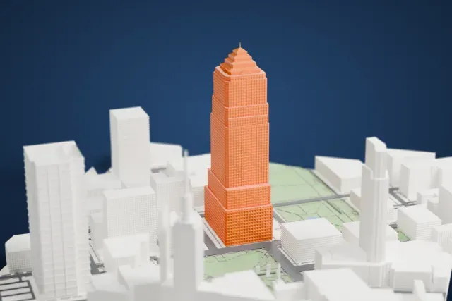 A white 3D print of Key Tower, a tall stepped skyscraper topped with a pyramid and thin spire, rising among the buildings and green squares of downtown Cleveland.